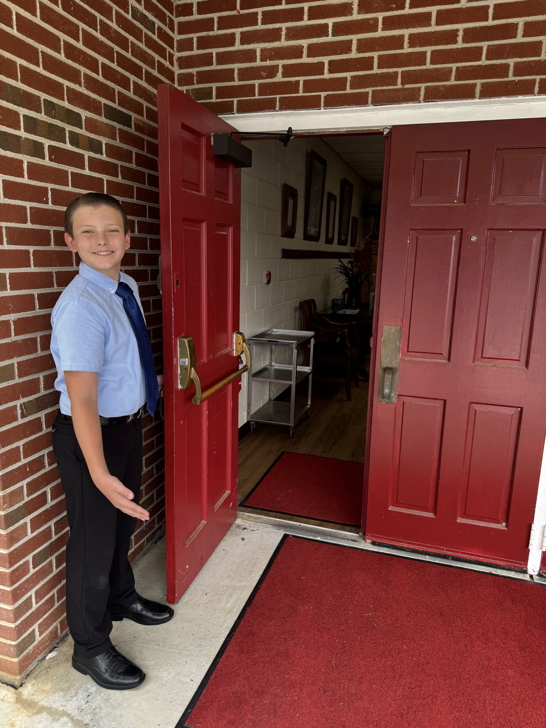 A young greeter welcomes visitors through the open red church doors